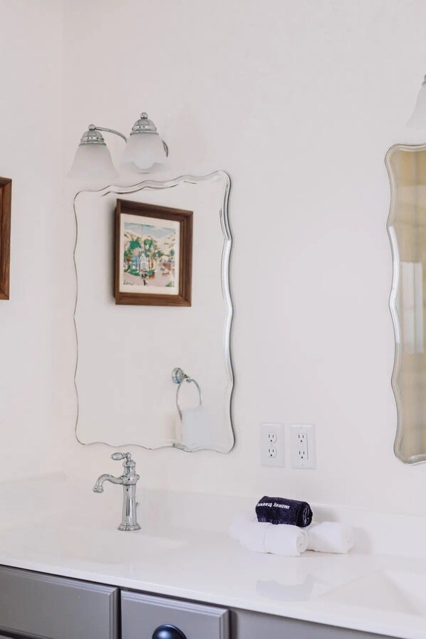 Un baño con un lavabo blanco, un espejo con marco ondulado, un cuadro en la pared y una toalla sobre la encimera.