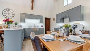 Een moderne keuken met grijze kastjes, een centraal eiland en een eethoek met een houten tafel voor vier personen.