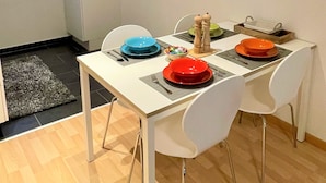 Un coin repas avec une table blanche, quatre chaises et une horloge au mur.