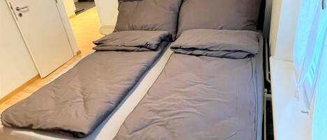 A bed with a dark headboard and grey bedding in a room with wooden flooring and a white door.