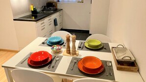 Une cuisine compacte avec des meubles blancs, une fenêtre agrémentée de rideaux et un coin repas avec une table mise pour deux personnes.