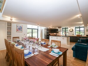 A modern kitchen with dark cabinets, a central island, and a dining area with a wooden table set for six. - Owl Barn (Leominster)