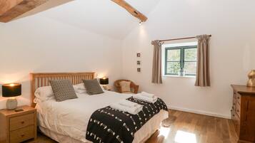 A bedroom with a wooden bed, a nightstand, a lamp, a window with curtains, and a wooden dresser.