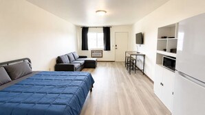 Un dormitorio con cama, sofá, una mesita, televisor y kitchenette.