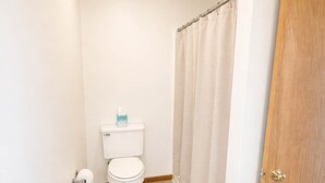 Un baño con inodoro, cortina de ducha y suelo de madera.