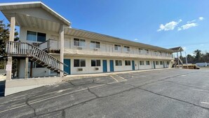 Un motel de dos pisos con una escalera central, un estacionamiento y un cielo azul despejado.