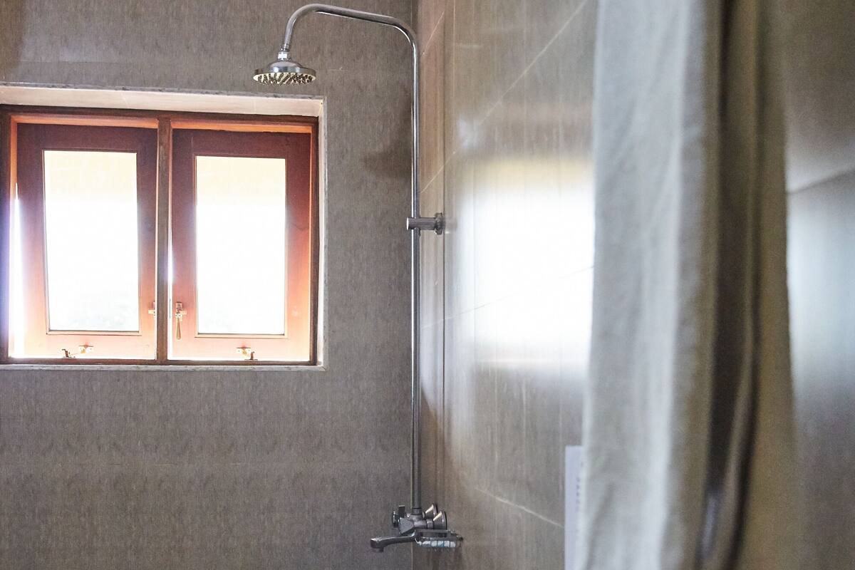 A bathroom with a shower, toilet, and a window with two panes.