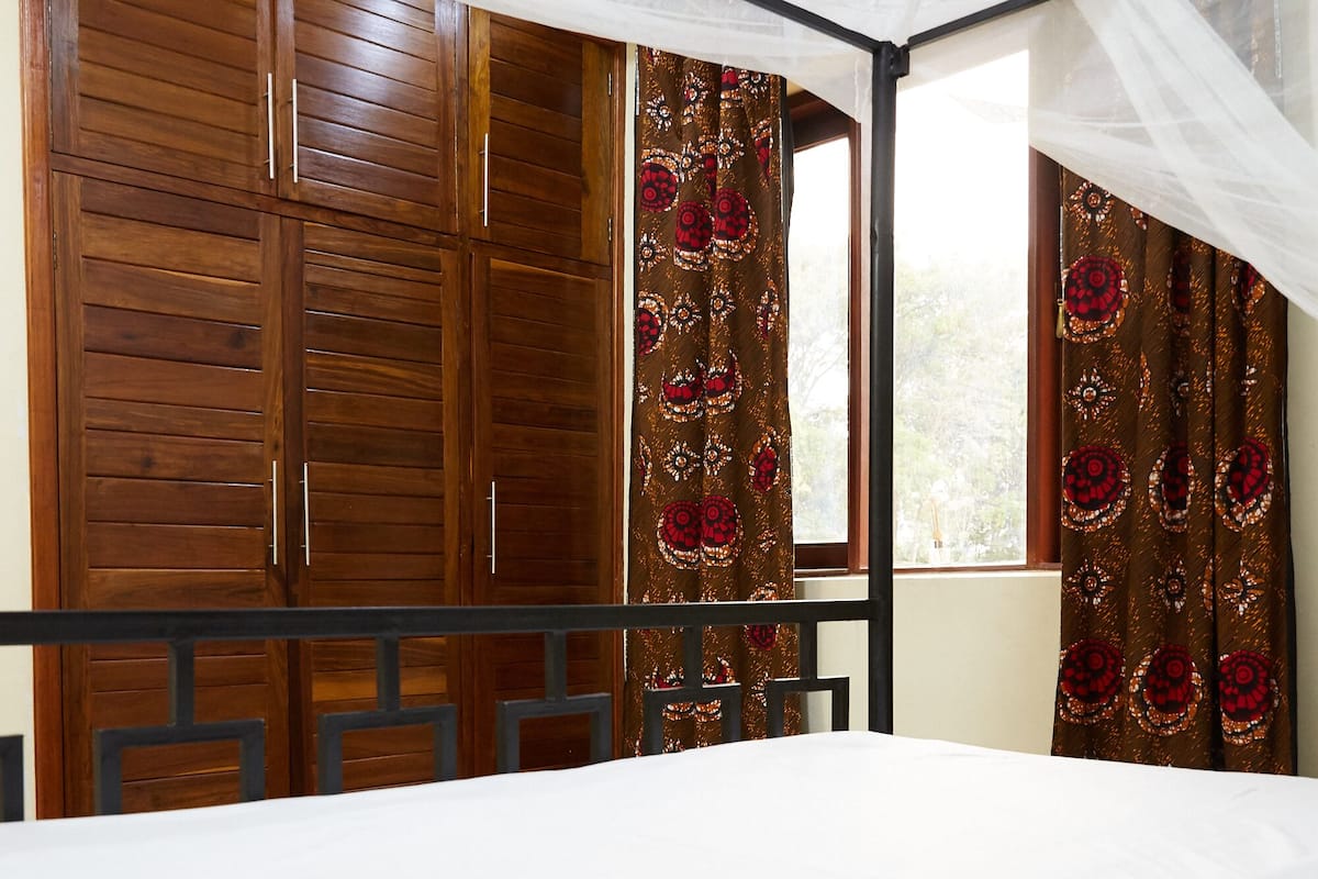 A bedroom with a bed, wooden wardrobe, and curtains.