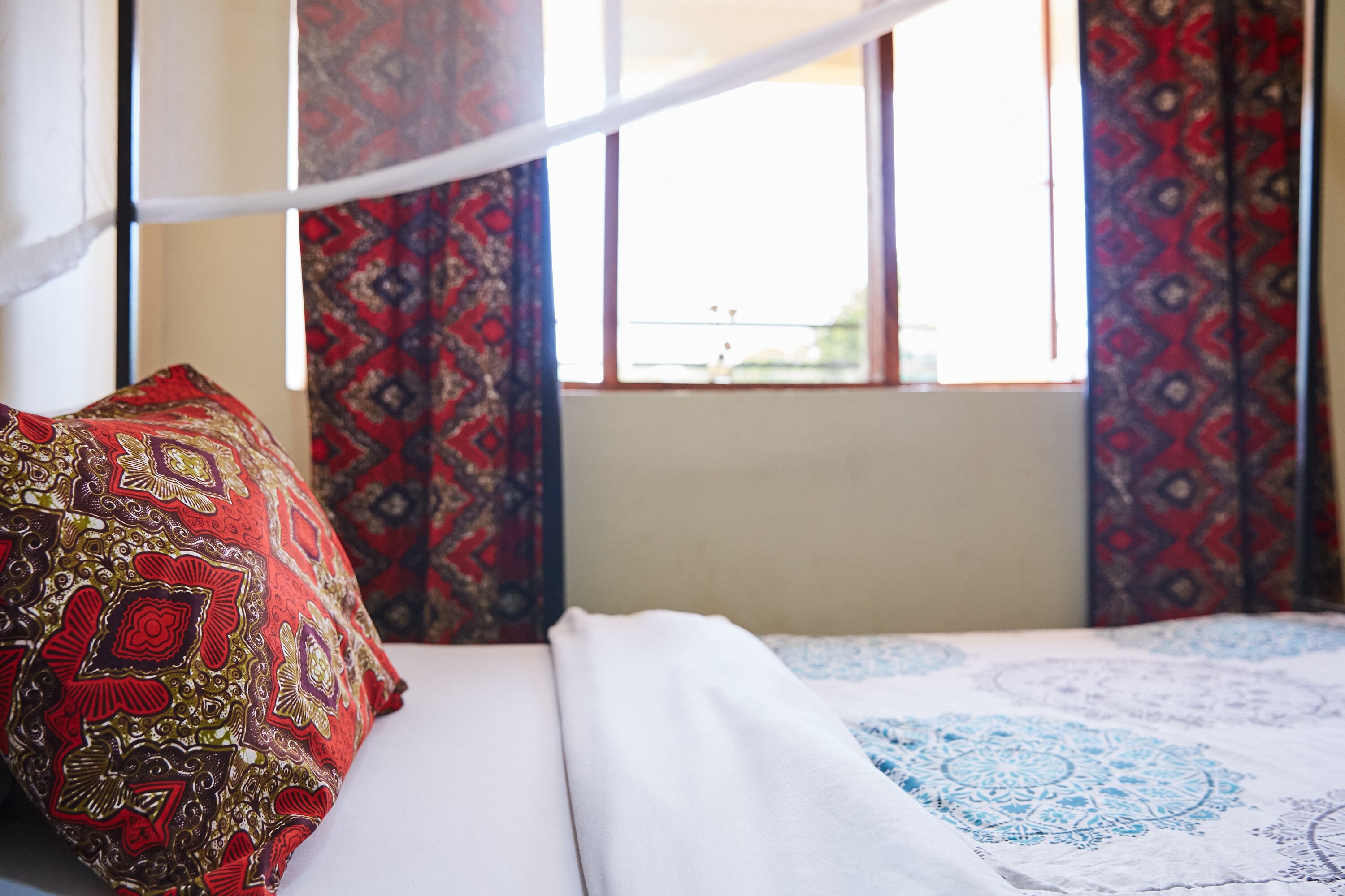 Un lit avec un oreiller rouge et doré à motifs, une couvre-lit blanche et une housse de lit bleue et blanche à motifs.