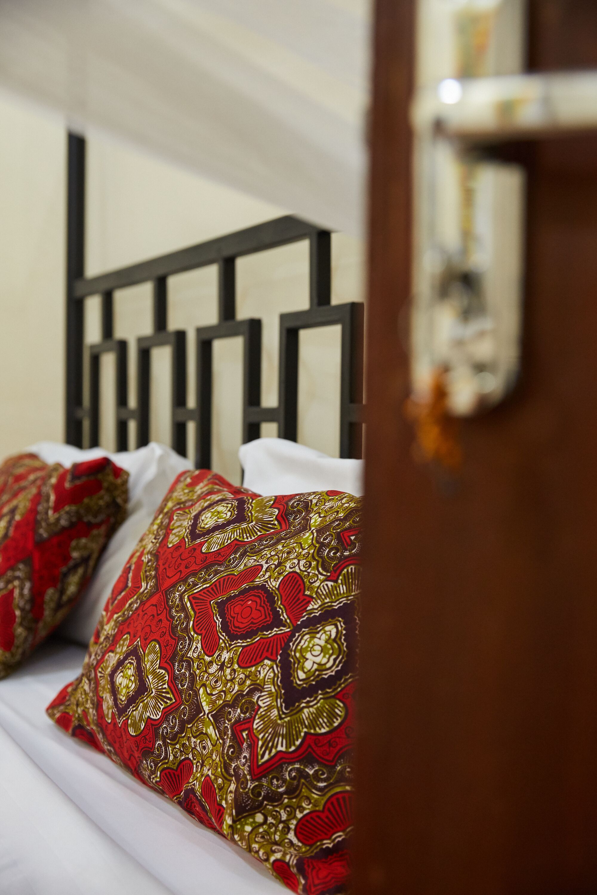 Cama com cabeceira de metal preto e almofadas com padrão vermelho e dourado.