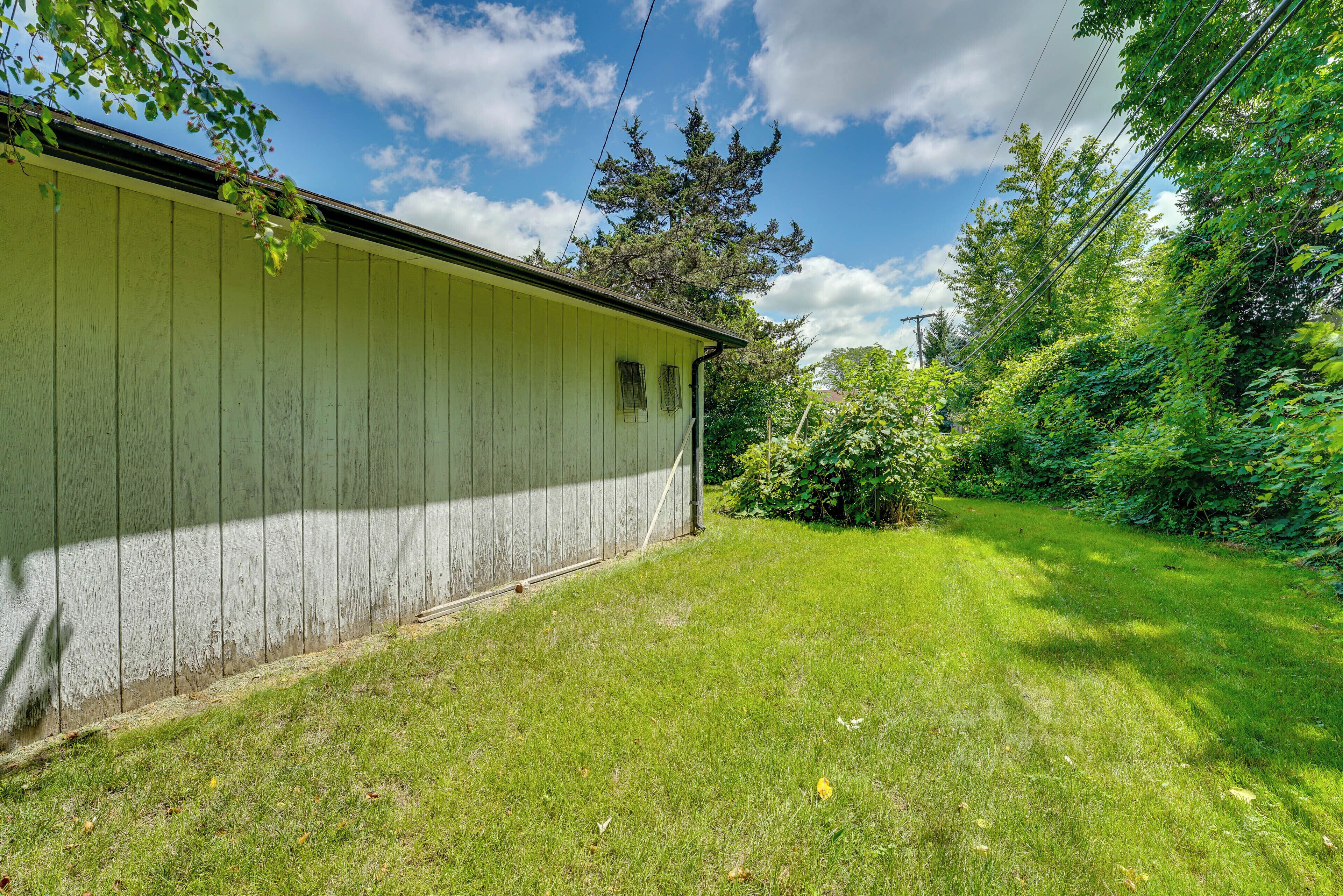 A green wooden building with a sloped roof, surrounded by a well-maintained lawn and dense greenery.