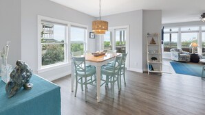 Una habitación amplia con una mesa de comedor y sillas, ventanas grandes que ofrecen vista a zonas verdes y un edificio, además de un ventilador de techo.