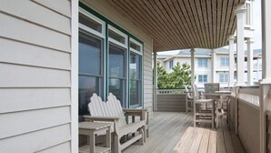 Un porche cubierto con sillas Adirondack y una mesa, terraza de madera y vista de edificios cercanos.