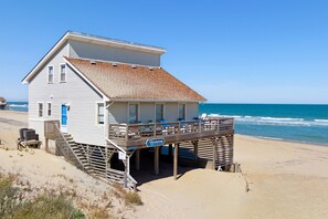 Une maison de plage avec un balcon, une terrasse en bois et un panneau indiquant qu’il s’agit d’un poste de surveillance des sauveteurs.