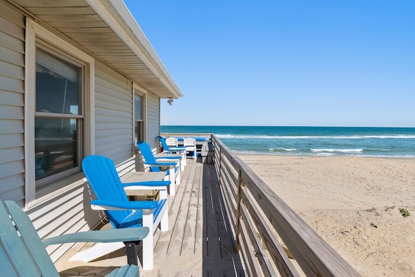 Une terrasse en bois avec des chaises et des tables bleues, donnant sur une plage.