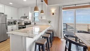 A modern kitchen with white cabinets, stainless steel appliances, a marble island, and bar stools. - Torchsong: Oceanfront, Direct Beach Access, Dogs OK (Nags Head)