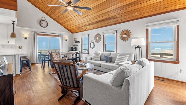 A spacious living area with a wooden ceiling, a dining table, a sofa, and a view of the ocean. - Torchsong: Oceanfront, Direct Beach Access, Dogs OK (Nags Head)