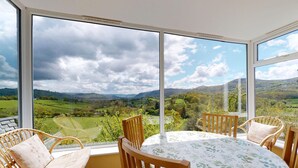 A room with a large window offering a scenic view of rolling hills and a cloudy sky. - Eryl - Three Bedroom Cottage, Sleeps 5 (Rowen)