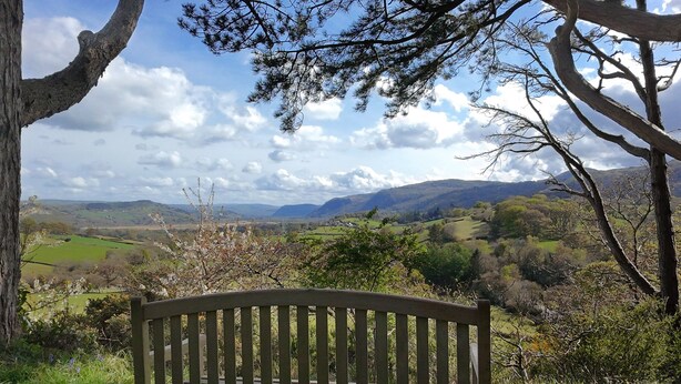 A wooden bench overlooking a scenic landscape with hills and a clear sky. - Eryl - Three Bedroom Cottage, Sleeps 5 (Rowen)