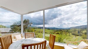 A room with a large window offering a view of a green landscape and cloudy sky. - Eryl - Three Bedroom Cottage, Sleeps 5 (Rowen)