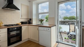 Cozinha moderna com fogão a gás, forno, lava-louças e uma janela grande com vista para o exterior.