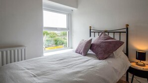 Quarto com cama, janela, radiador e mesa de cabeceira com abajur.