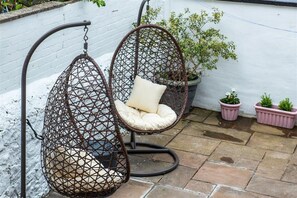 Two hanging chairs with cushions, a white brick wall, potted plants, and stone flooring.