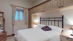 A bedroom with a bed, nightstands, a dresser, a window with curtains, and wooden cabinets above the bed.