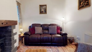 A living room with a brown leather sofa, a patterned rug, a wooden coffee table, a side table with a lamp, and a fireplace.