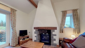 A living room with a stone fireplace, a television on a wooden stand, a leather sofa, and patterned curtains.