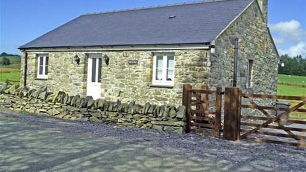 A stone house with a sloped roof, a wooden gate, and a stone wall in front.