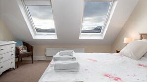 A bedroom with two skylights, a bed with white linens, a chair, a dresser, and a nightstand with a lamp. - The Barn - One Bedroom Cottage, Sleeps 2 (Bala)