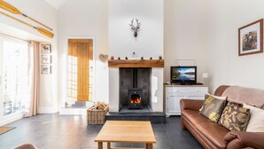 A living room with a fireplace, a sofa, a TV, and a wooden table. - The Barn - One Bedroom Cottage, Sleeps 2 (Bala)