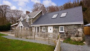 A stone house with a sloped roof, multiple windows, and a wooden fence. - The Barn - One Bedroom Cottage, Sleeps 2 (Bala)