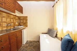 Una cucina compatta con mobili in legno, zoccolo in piastrelle, lavastoviglie integrata e una piccola finestra con tende.
