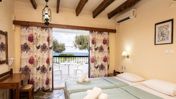 Un dormitorio con dos camas, un escritorio de madera, una silla y un balcón con vista al mar.