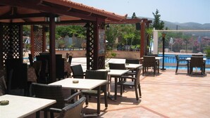 Un patio al aire libre con mesas y sillas, una piscina al fondo y vistas a las colinas.