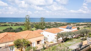 Un área residencial costera con casas de tejados de terracota, olivos y vistas al mar.