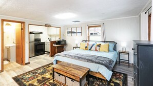 A bedroom with a bed, bedside table, and a dresser. There is a kitchen area with a stove and sink.