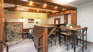 A rustic interior with a wooden bar, stone wall, and a cozy seating area with a couch and chairs.