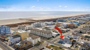 Luftaufnahme einer Küstenstadt mit Strand, mit einer Mischung aus Wohn- und Geschäftshäusern, darunter ein Hotel, das durch einen großen roten Pfeil hervorgehoben wird.