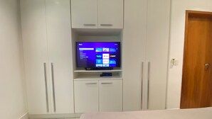 Een slaapkamer met een bed, een televisie bevestigd aan een witte kast, en een houten deur.