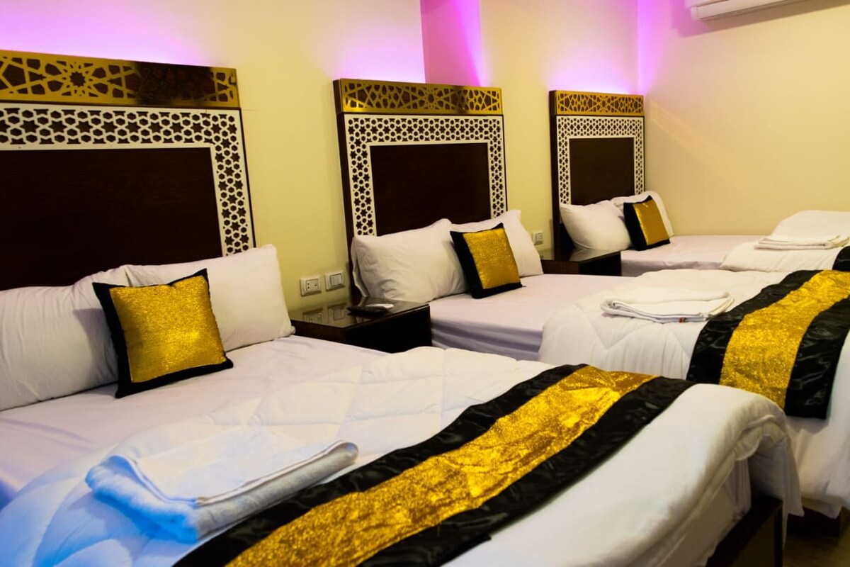 A hotel room with three beds, each with white bedding and gold accents.