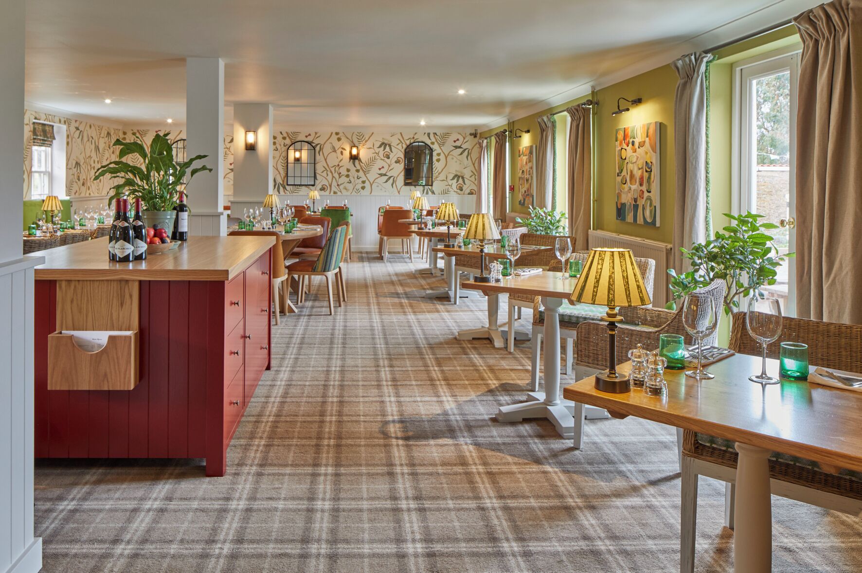 Un restaurant avec un sol à carreaux, des tables et des chaises en bois. On y trouve des plantes en pot et un coin bar avec des bouteilles.
