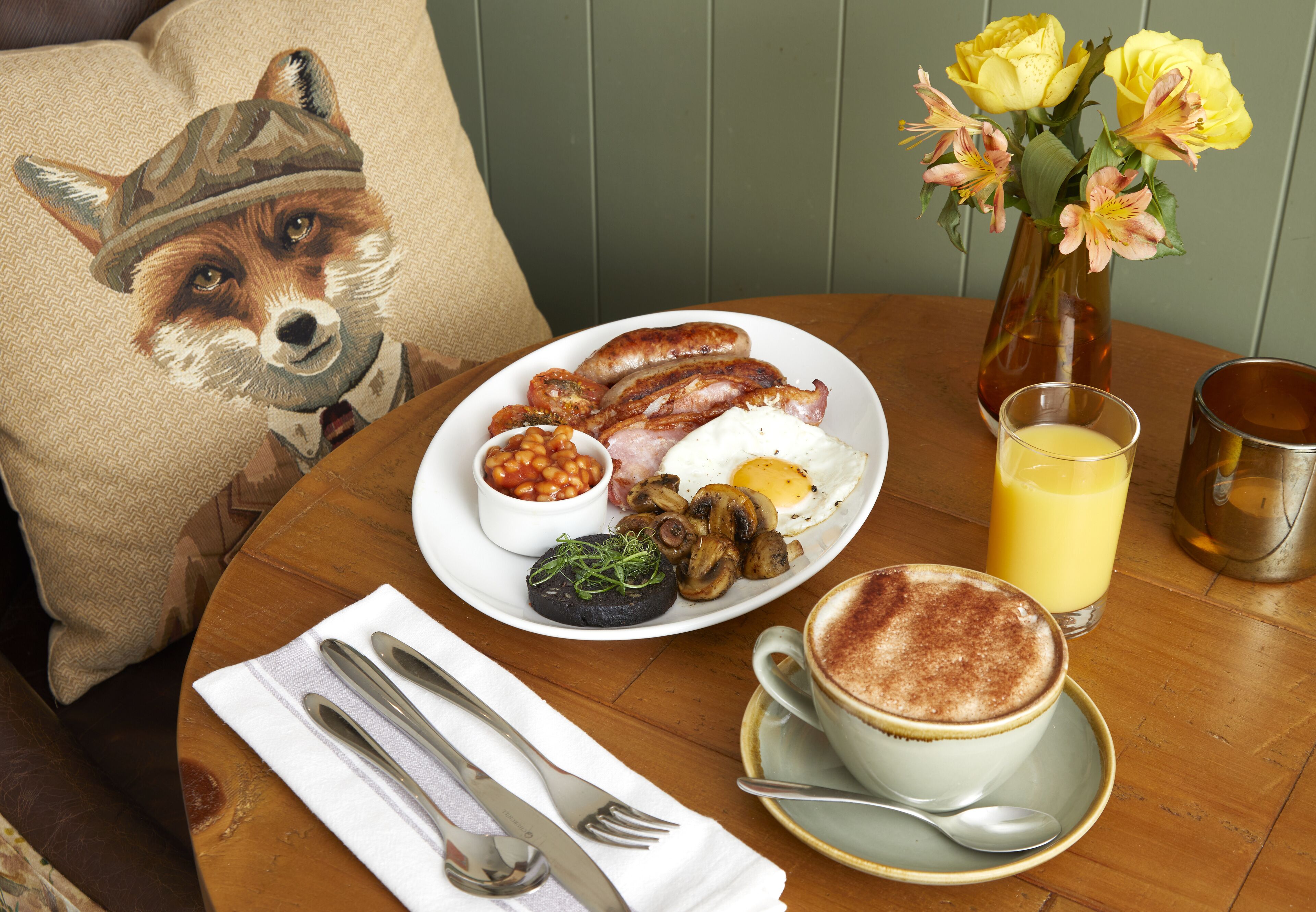 A breakfast table with a plate of food, a cup of coffee, and a vase of flowers.