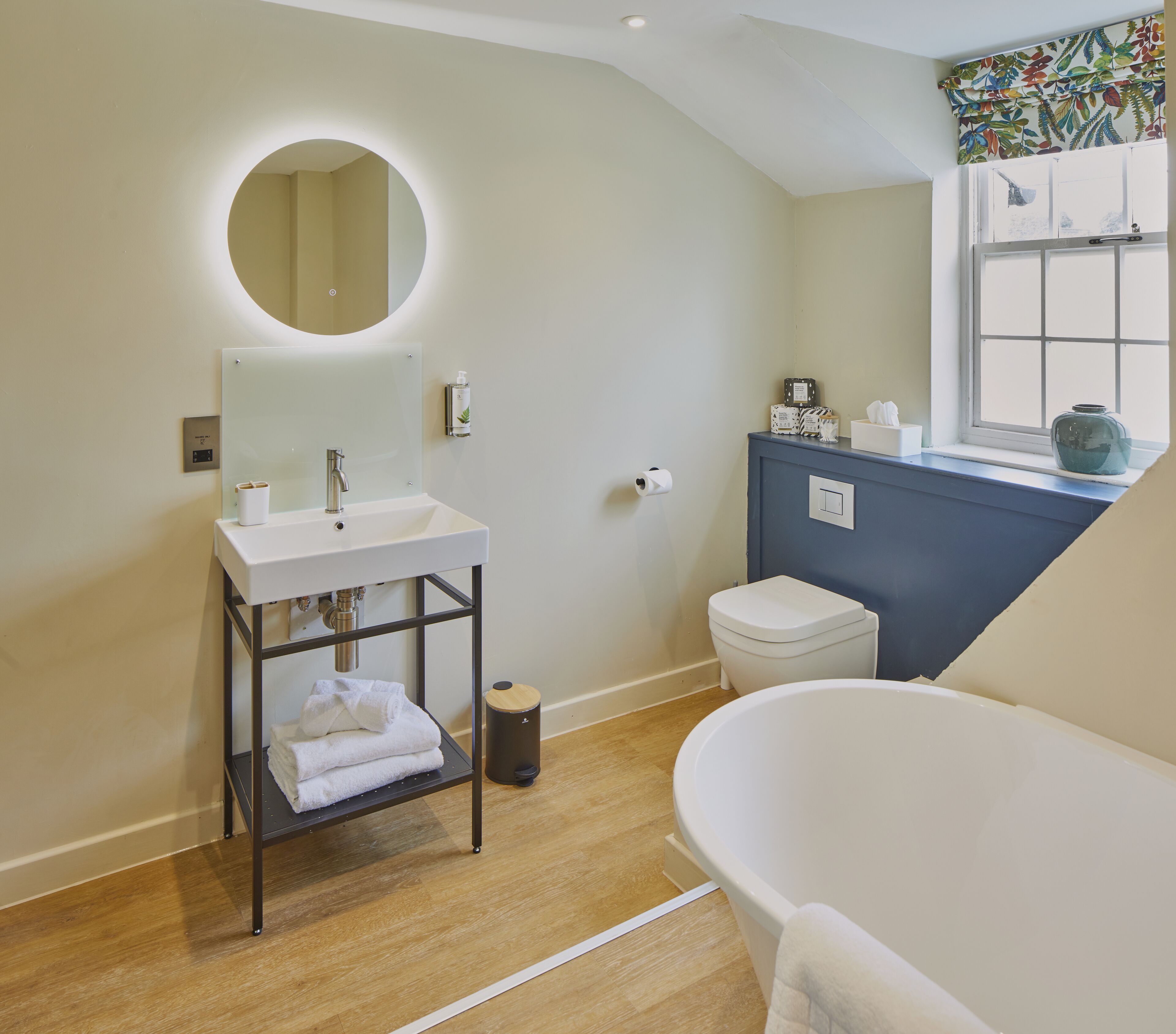 A bathroom with a white sink, round mirror, and a bathtub.