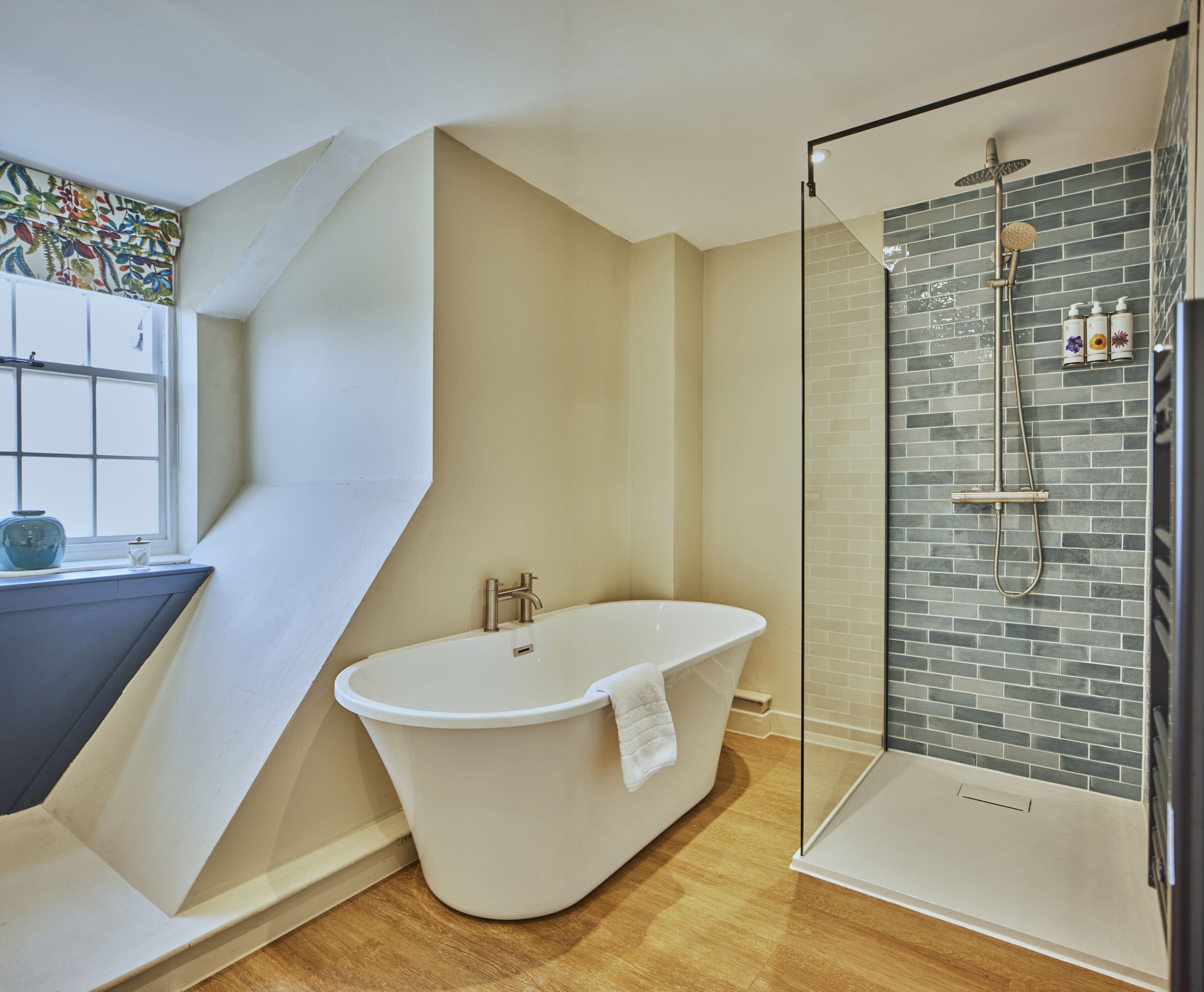 A modern bathroom with a freestanding bathtub, a glass-enclosed shower, and a window with a decorative curtain.