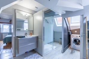 Une chambre moderne dotée d’une armoire intégrée, d’une cabine de douche en verre, d’un lave-linge et d’un puits de lumière.