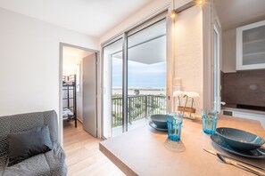 Un salon moderne avec un canapé, une table à manger agrémentée de verrerie bleue, et une vue sur la mer grâce à de grandes portes coulissantes.