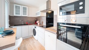 Une cuisine moderne avec des meubles blancs, un lave-linge encastré, un four en acier inoxydable et une grande fenêtre.